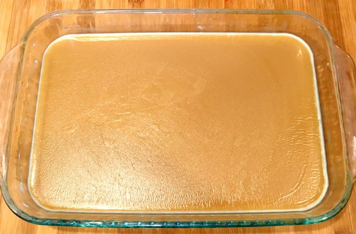 A process photo showing homemade microwave caramel setting in a glass Pyrex dish on a wooden counter