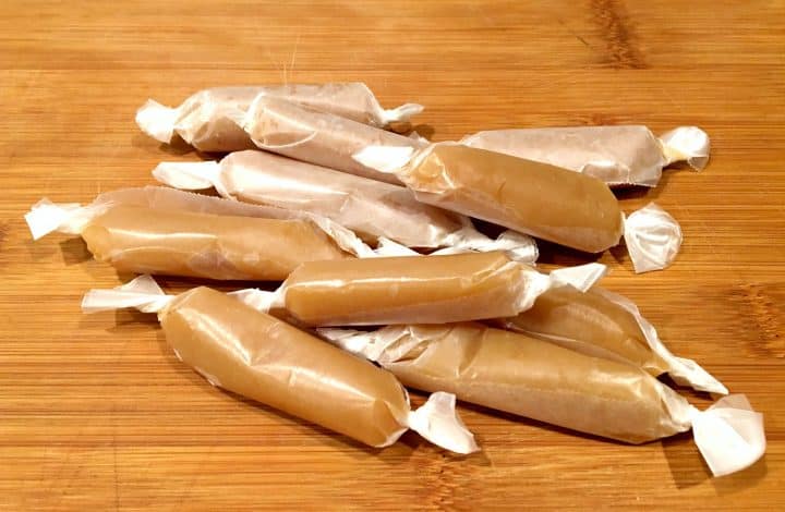 Homemade microwave caramels wrapped in wax paper on a wooden counter