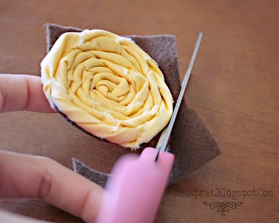 A process shot showing a hand trimming the felt backing of a homemade rolled fabric rosette