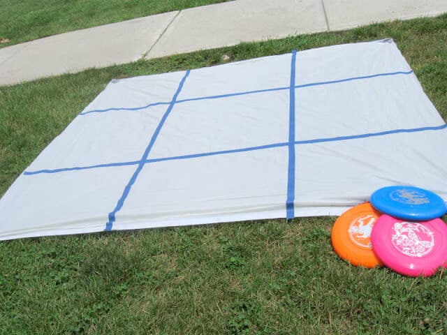 A game board to play backyard frisbee tic tac toe is made out of a shower curtain and painters tape and is set on a green lawn